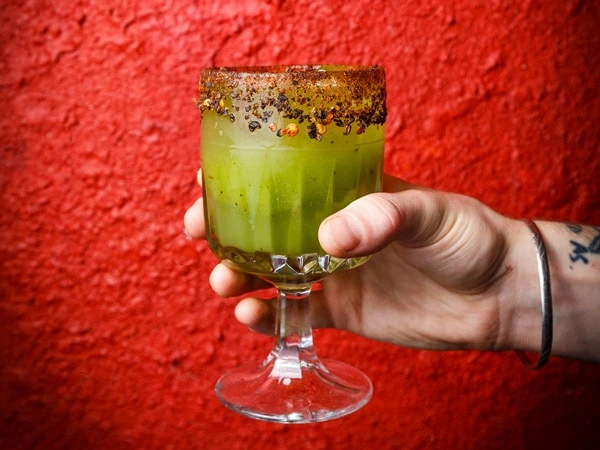 A picture of a green cocktail with chilli around the rim against a red background at Bodega Undeground Melbourne.