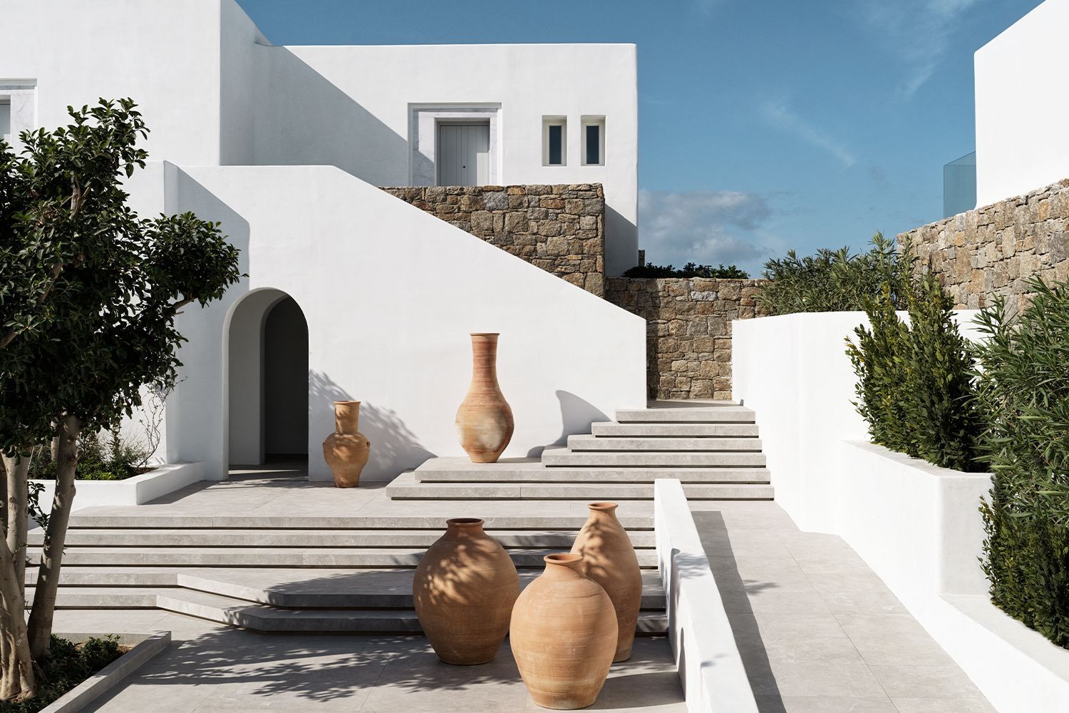 exterior of Deos Mykonos on the island of Mykonos with earthenware pots in the foreground and stairs.